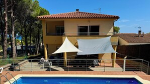 Une piscine avec une terrasse carrelée, un espace extérieur couvert avec des sièges, et un bâtiment avec un toit carrelé en arrière-plan.