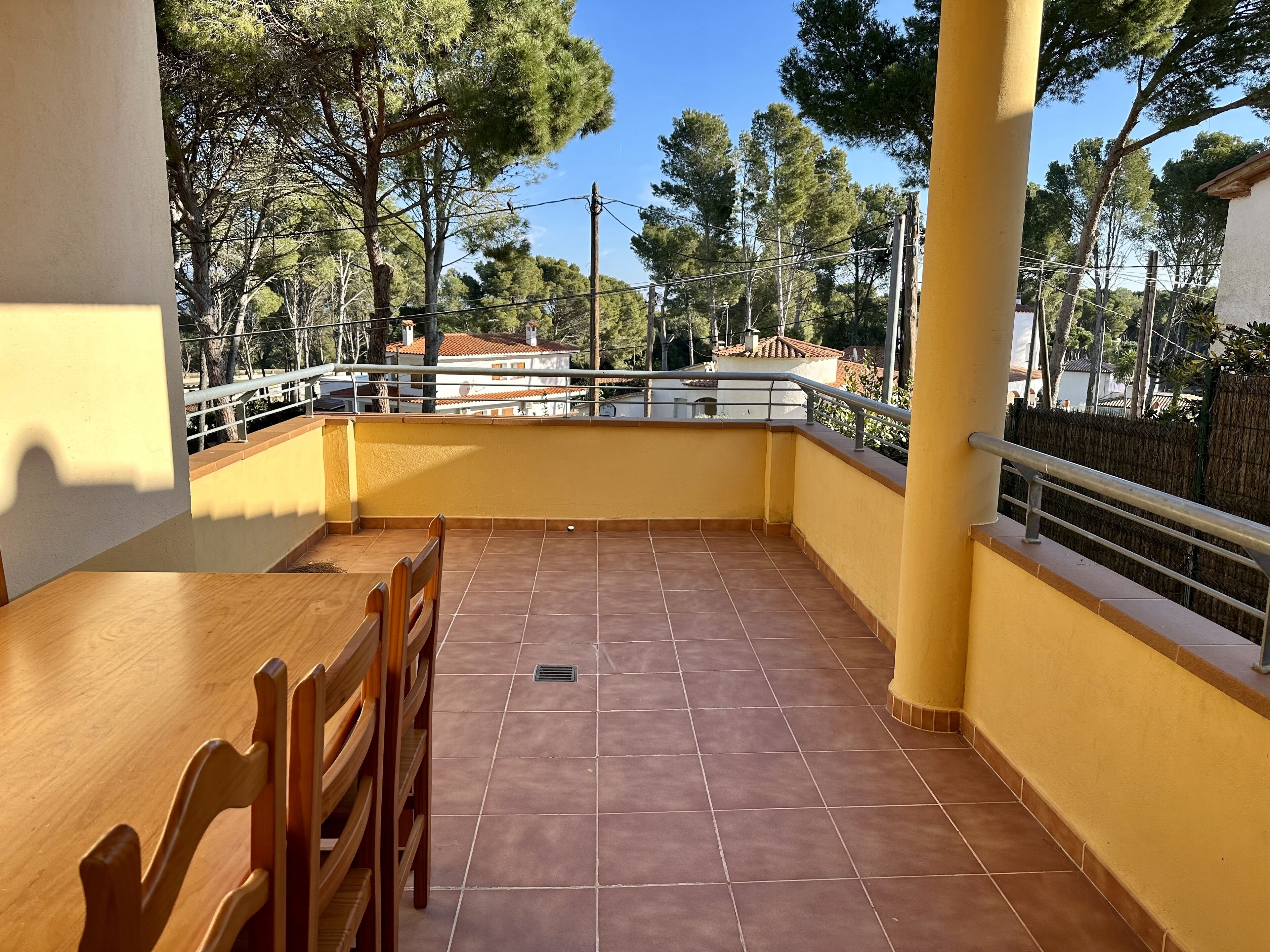 A balcony with tiled flooring, wooden chairs, and a railing.