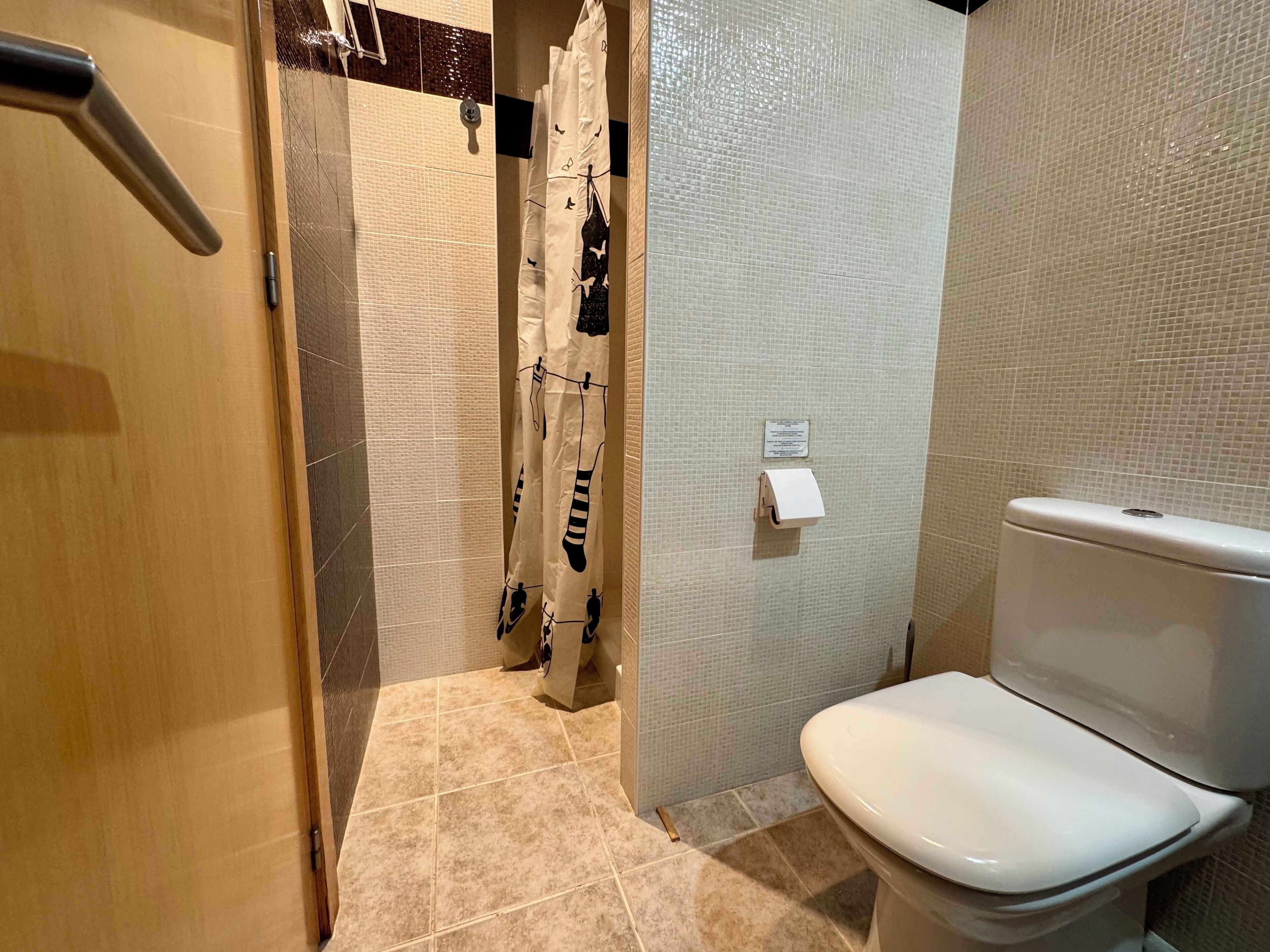 Une salle de bain avec des toilettes, une douche dotée d’un rideau à motifs et des murs carrelés.