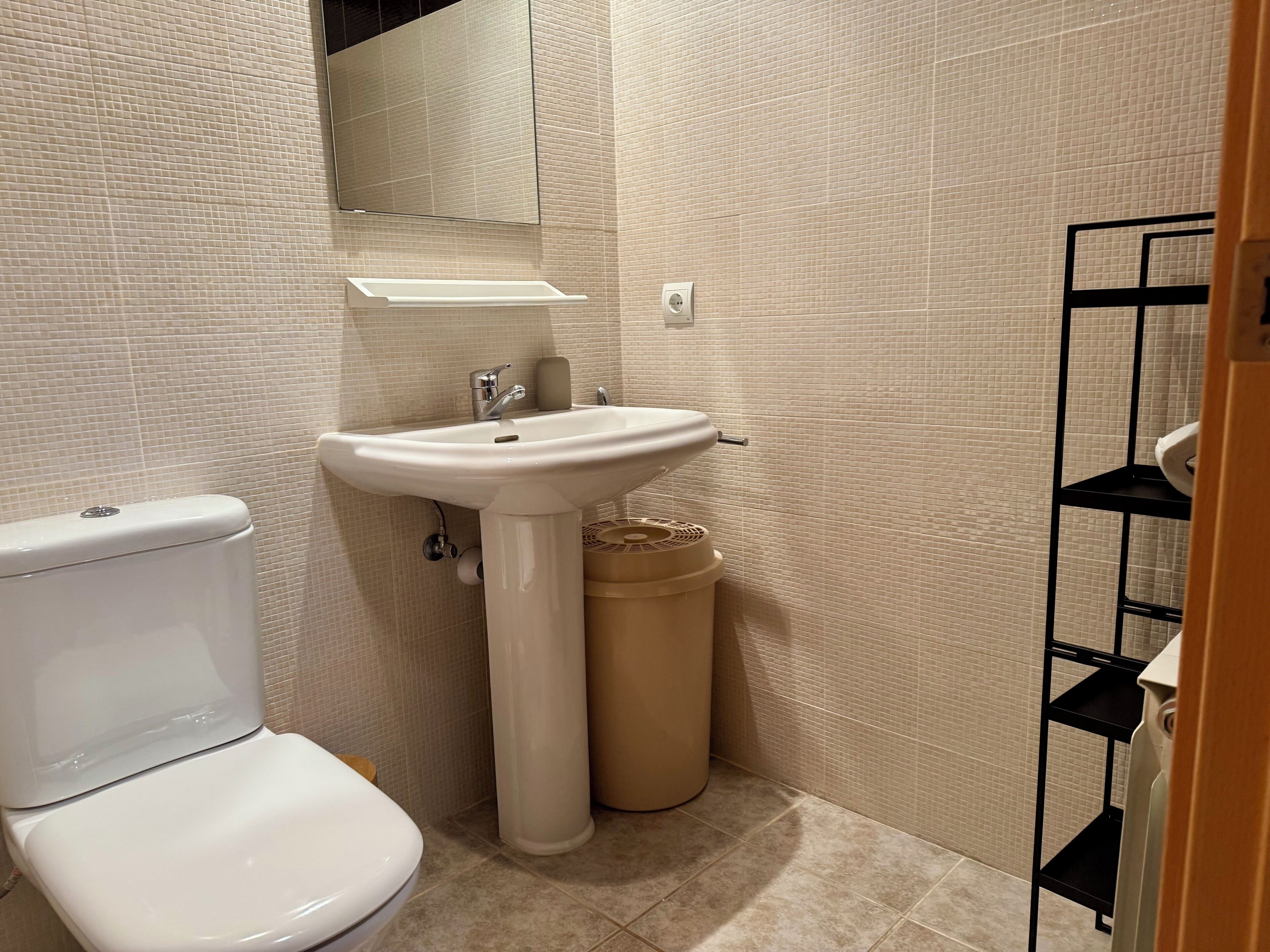 A bathroom with a toilet, sink, mirror, and tiled walls.