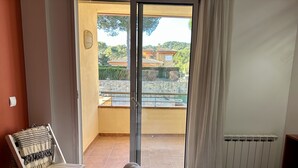 Une chambre avec un lit, une chaise, une fenêtre donnant sur une piscine et des bâtiments, et un radiateur.