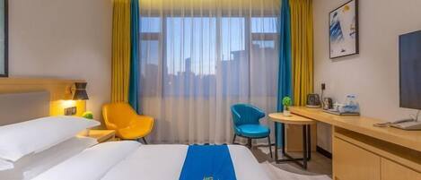 Ein Hotelzimmer mit Bett, Schreibtisch, Stuhl, einem kleinen Tisch und einem Fenster mit Vorhängen.