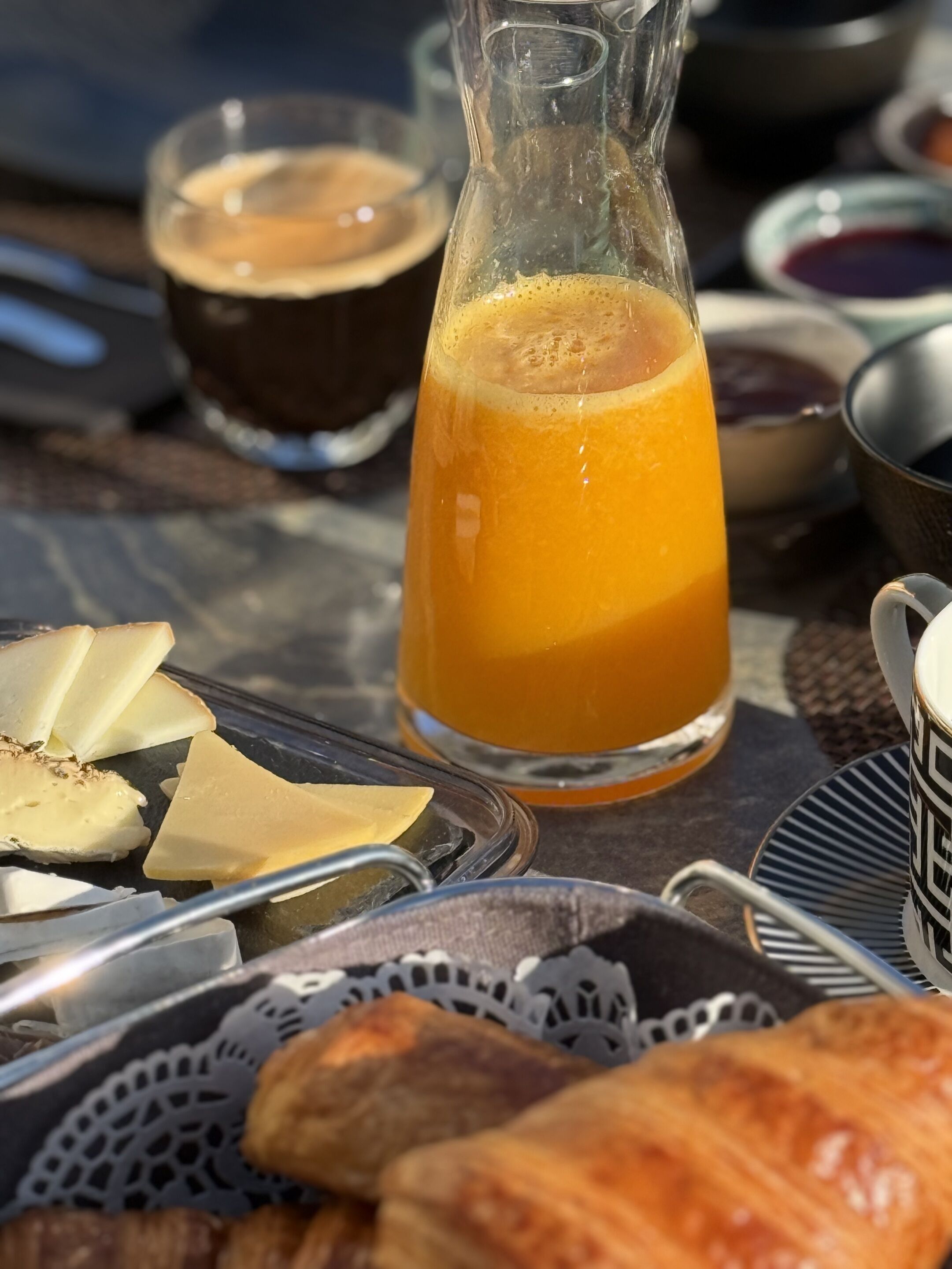 Una mesa con desayuno: un jarro de jugo de naranja, una taza de café y varias piezas de pastelería.