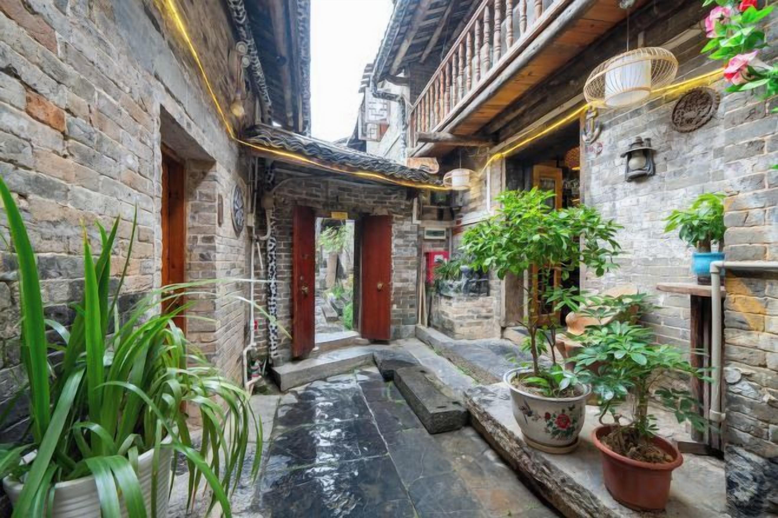 A narrow alleyway with traditional architecture, potted plants, and a small water feature.