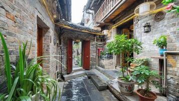 A narrow alleyway with traditional architecture, potted plants, and a small water feature.
