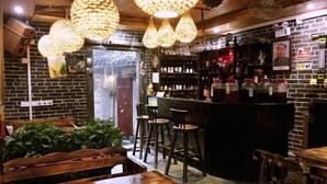 A bar area with wooden furniture, hanging light fixtures, and shelves with bottles. - By Chance Bar&Inn (Zhaoping)