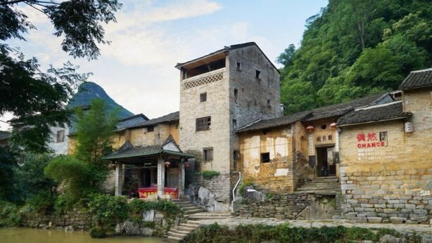 A traditional stone building with a tower, a small pavilion, and a sign indicating a family lodge. - By Chance Bar&Inn (Zhaoping)