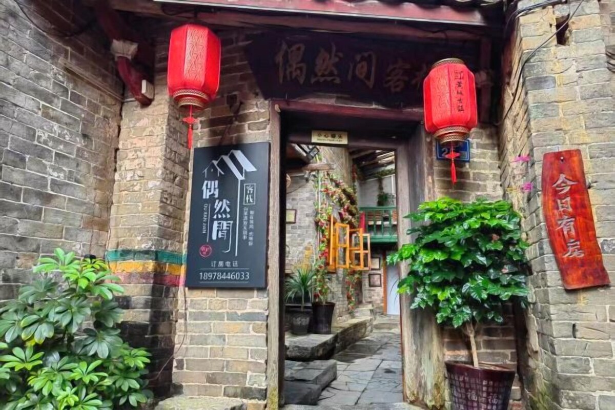 A traditional Chinese entrance with red lanterns, a signboard, and a brick wall.