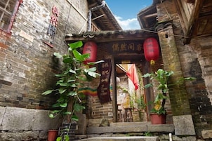 Un estrecho callejón con una entrada tradicional china, muros de ladrillo y faroles rojos colgantes.