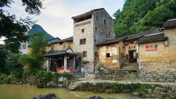 A traditional stone building with a central tower, a small bridge, and a river in the foreground.