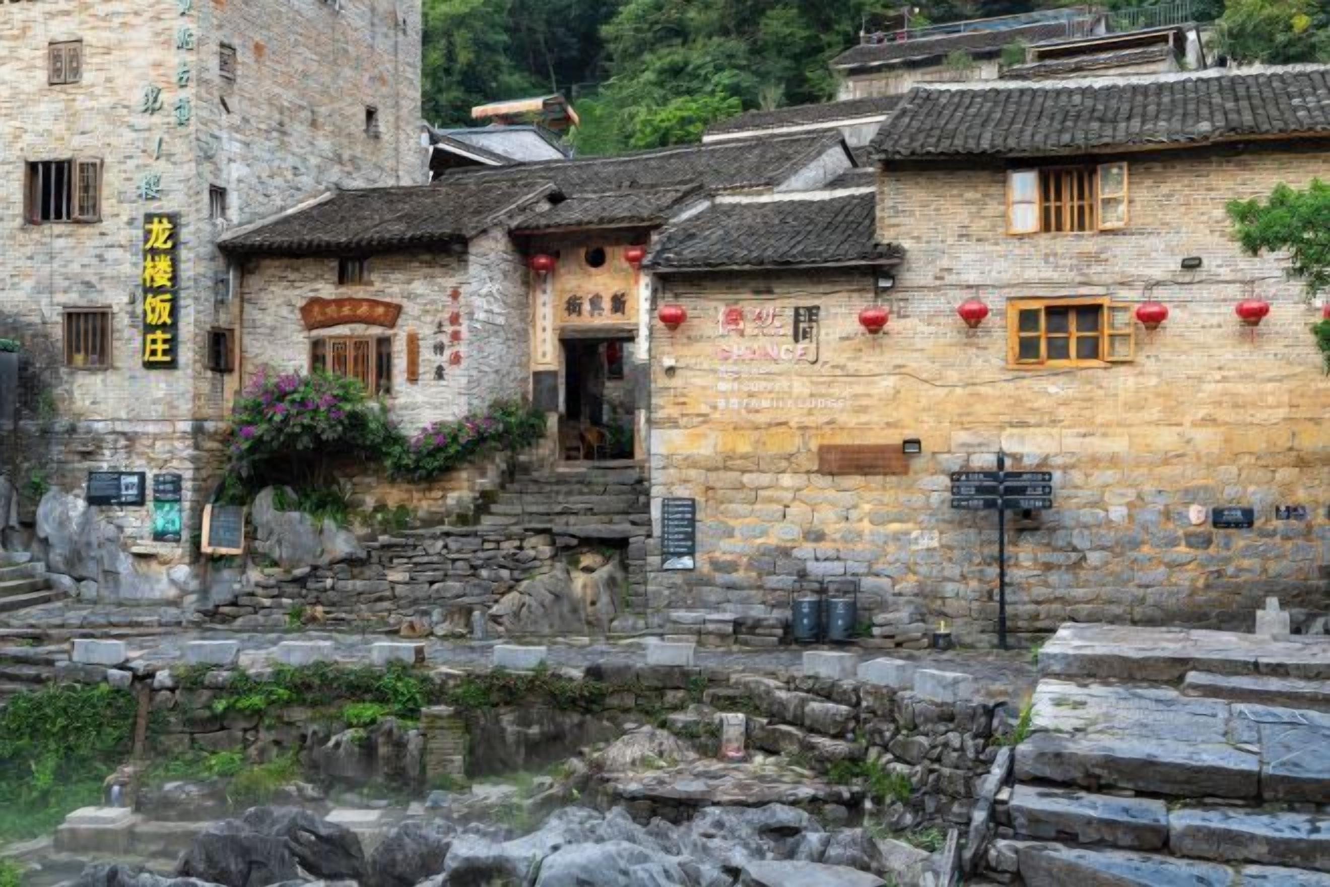 A traditional stone building with a staircase leading to a door, surrounded by stone walls and a small water feature.