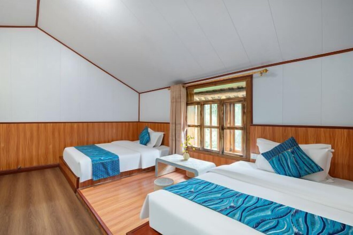A hotel room with two single beds, a small table, and a window with curtains.