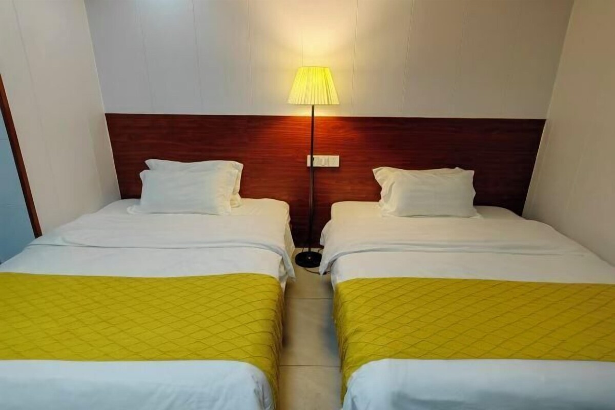 A hotel room with two beds, a wooden headboard, a nightstand, and a single bedside lamp.