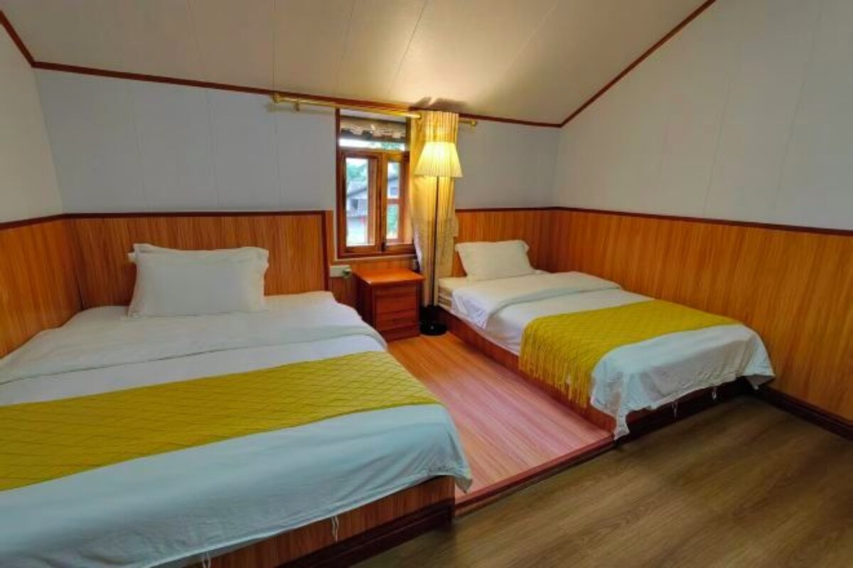 A room with two beds, wooden paneling, a window with curtains, and a nightstand.