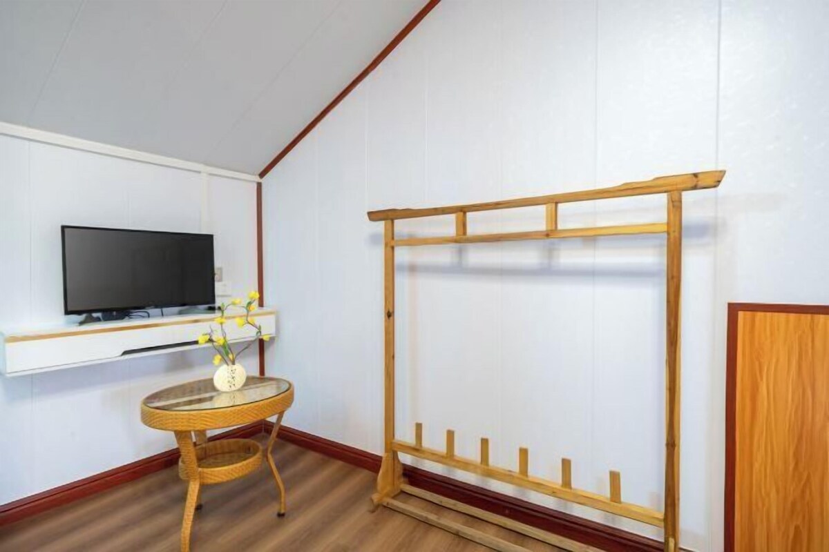 A room with a TV mounted on the wall, a small round table with a vase of flowers, and a wooden rack against the wall.