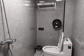 A bathroom with a toilet, a trash bin, a shower head, and a soap dispenser. - By Chance Bar&Inn (Zhaoping)