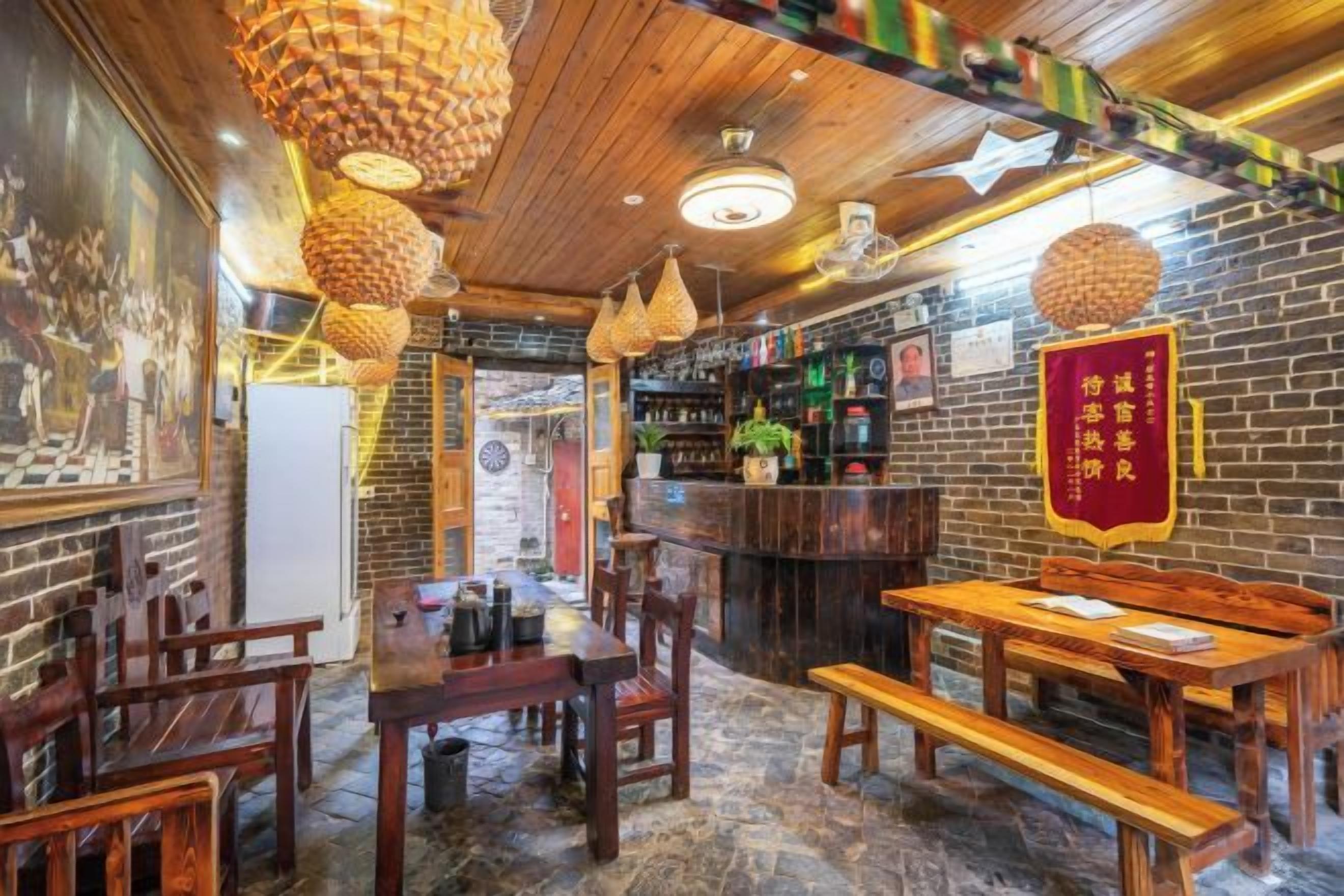 A restaurant interior with wooden tables and chairs, hanging light fixtures, and a brick wall.