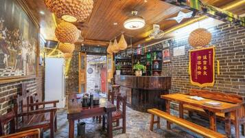 A restaurant interior with wooden tables and chairs, hanging light fixtures, and a brick wall.