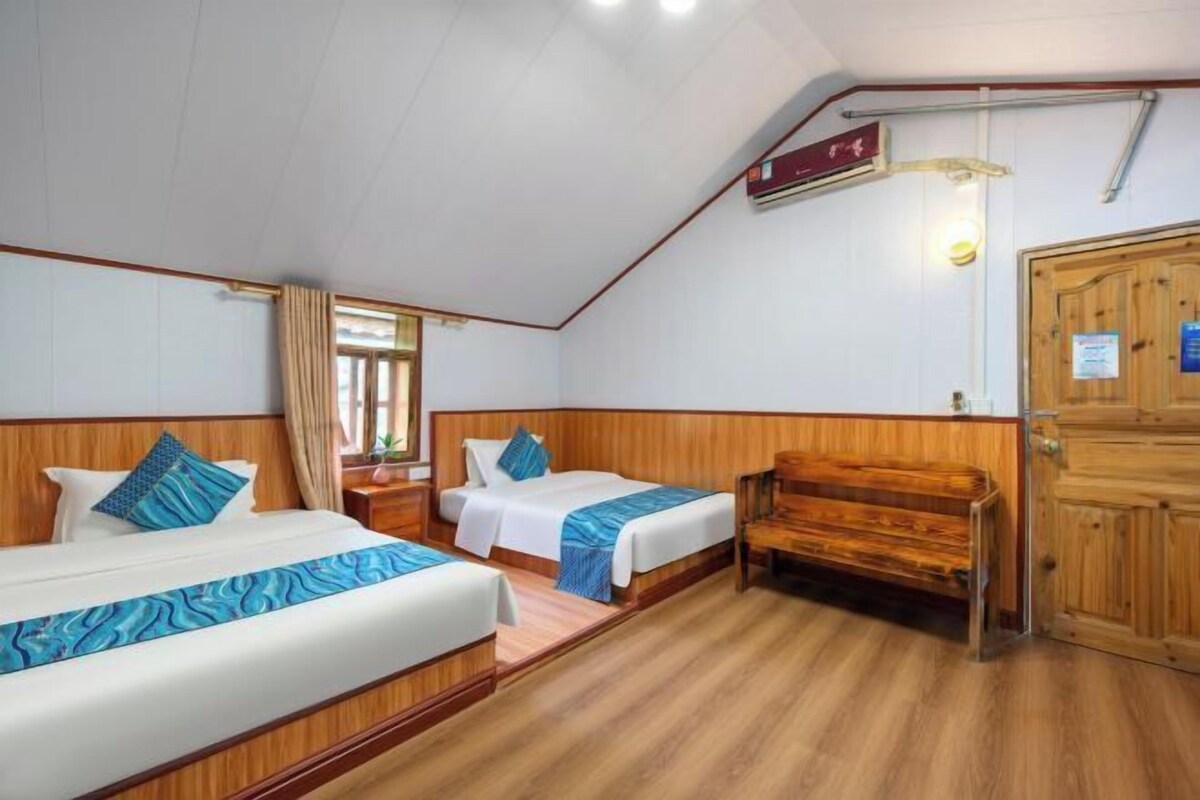 A room with two beds, a wooden bench, a wardrobe, and a window with curtains.