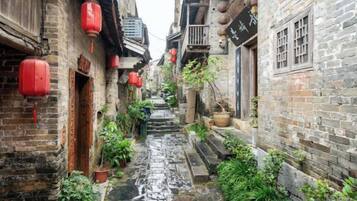 Un callejón estrecho con edificios de ladrillo, faroles rojos y plantas en macetas.