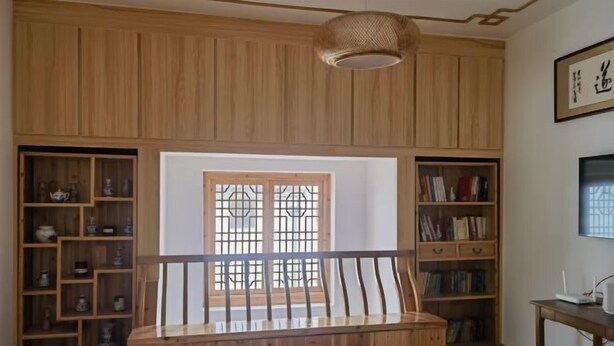 A room with a wooden bench, wooden shelves with decorative items, a window with a traditional design, and a wall-mounted television. - Guankeng Hotel (Wuyuan)