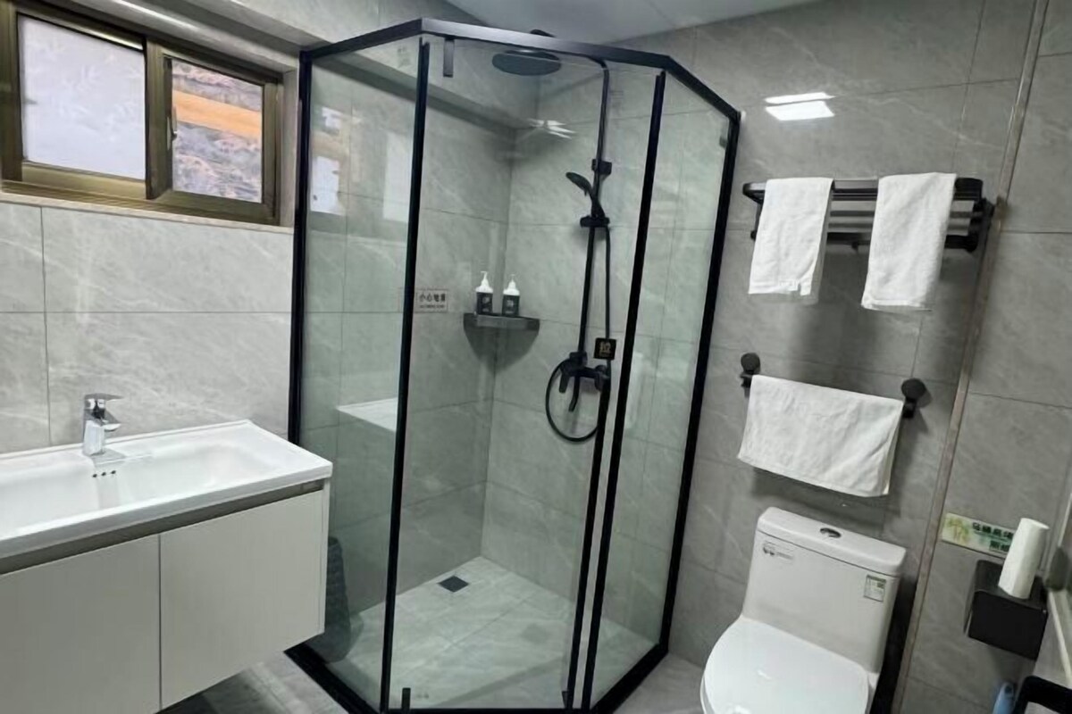 A modern bathroom with a glass-enclosed shower, a white sink, and a toilet.