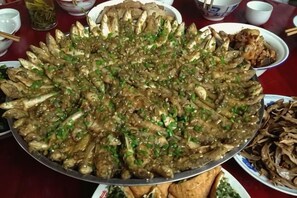A large platter of cooked seafood, likely a traditional dish, surrounded by smaller bowls of food and utensils on a table. - Guankeng Hotel (Wuyuan)