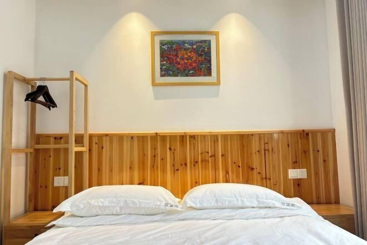 Un dormitorio con cabecera de madera, cama con ropa de cama blanca, estante de madera con ropa y un cuadro enmarcado en la pared.
