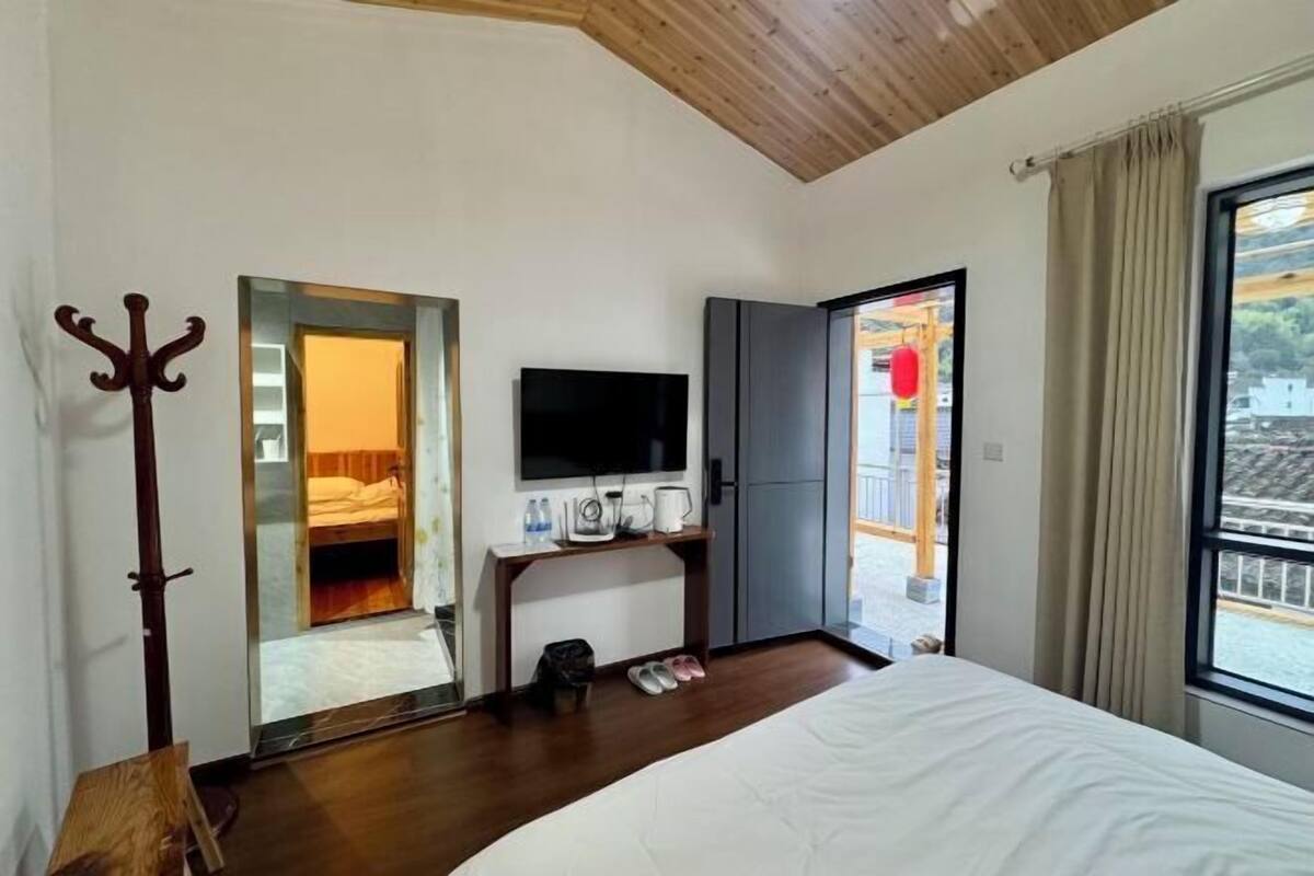 Una habitación de hotel moderna con una cama grande, un televisor de pantalla plana, un perchero de madera y vistas al exterior.