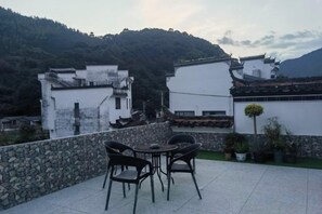 A terrace with a table and chairs, overlooking a mountainous area with traditional buildings. - Guankeng Hotel (Wuyuan)