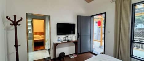 A bedroom with a bed, a TV, a desk, and a window with curtains.
