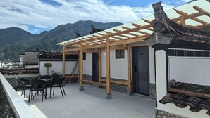 A traditional-style building with a wooden pergola, a tiled patio, and a view of mountains. - Guankeng Hotel (Wuyuan)