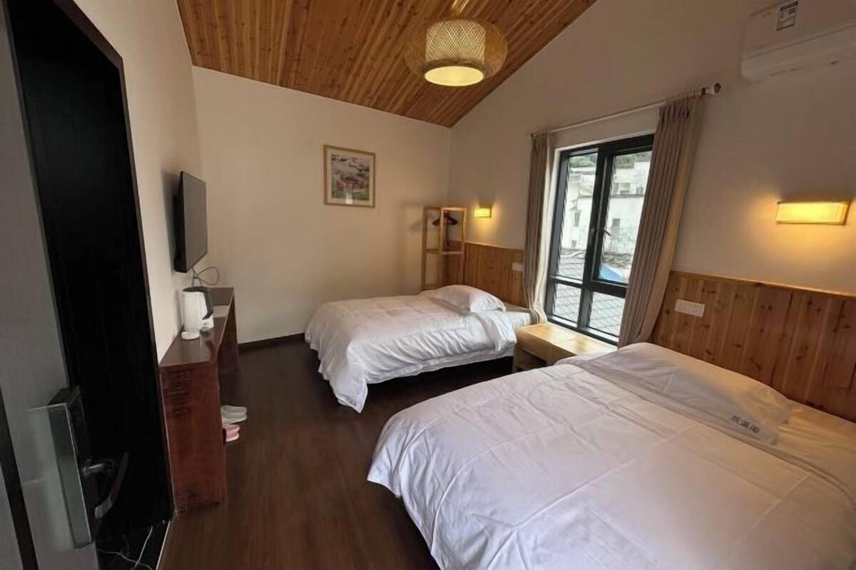 Habitación de hotel con dos camas, techo de madera, televisión, escritorio con silla y ventana con cortinas.