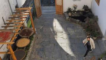 A narrow stone pathway leading to a traditional entrance, surrounded by potted plants and a wooden ladder with baskets.