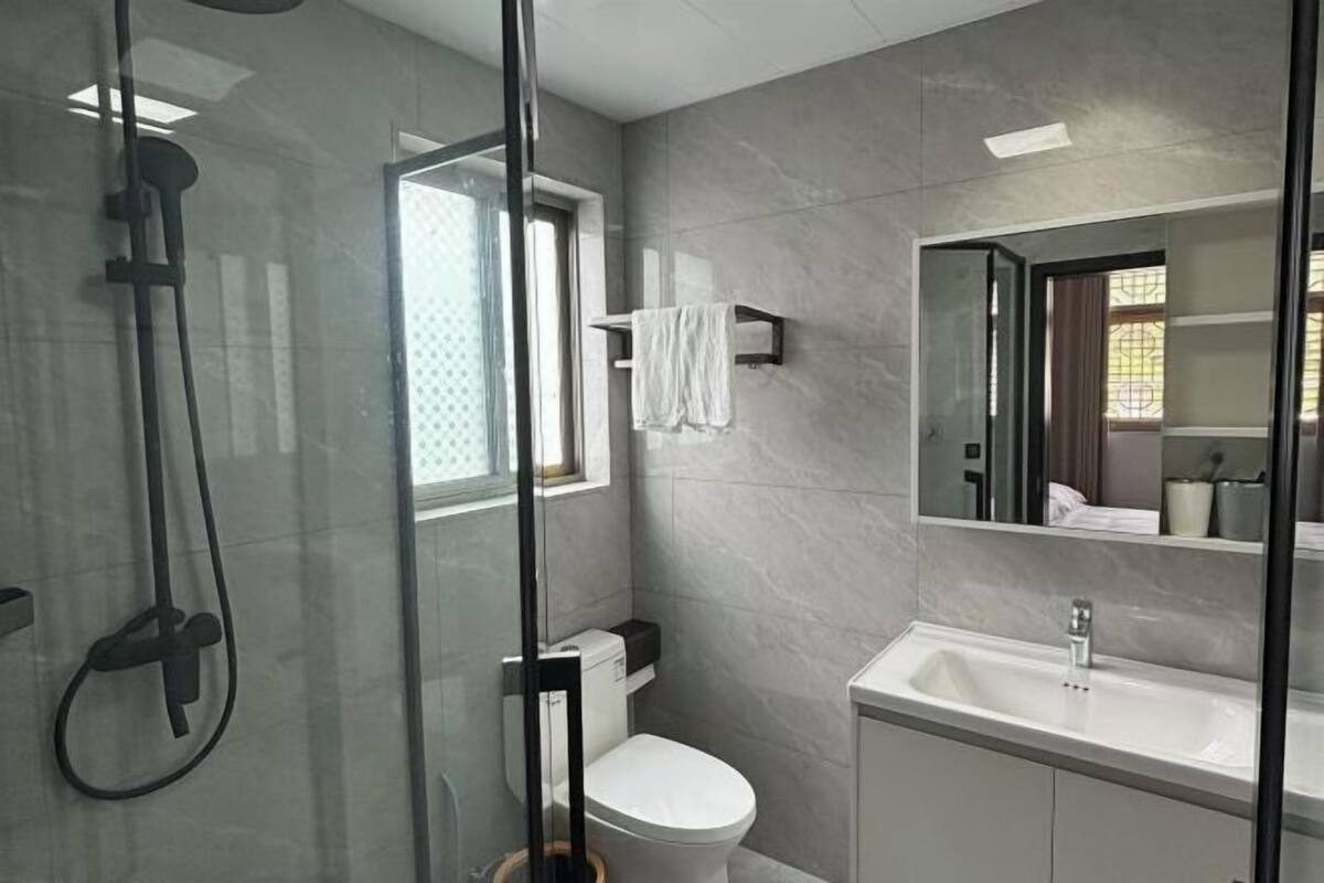 Un baño moderno con ducha de vidrio, inodoro blanco y lavamanos con espejo.