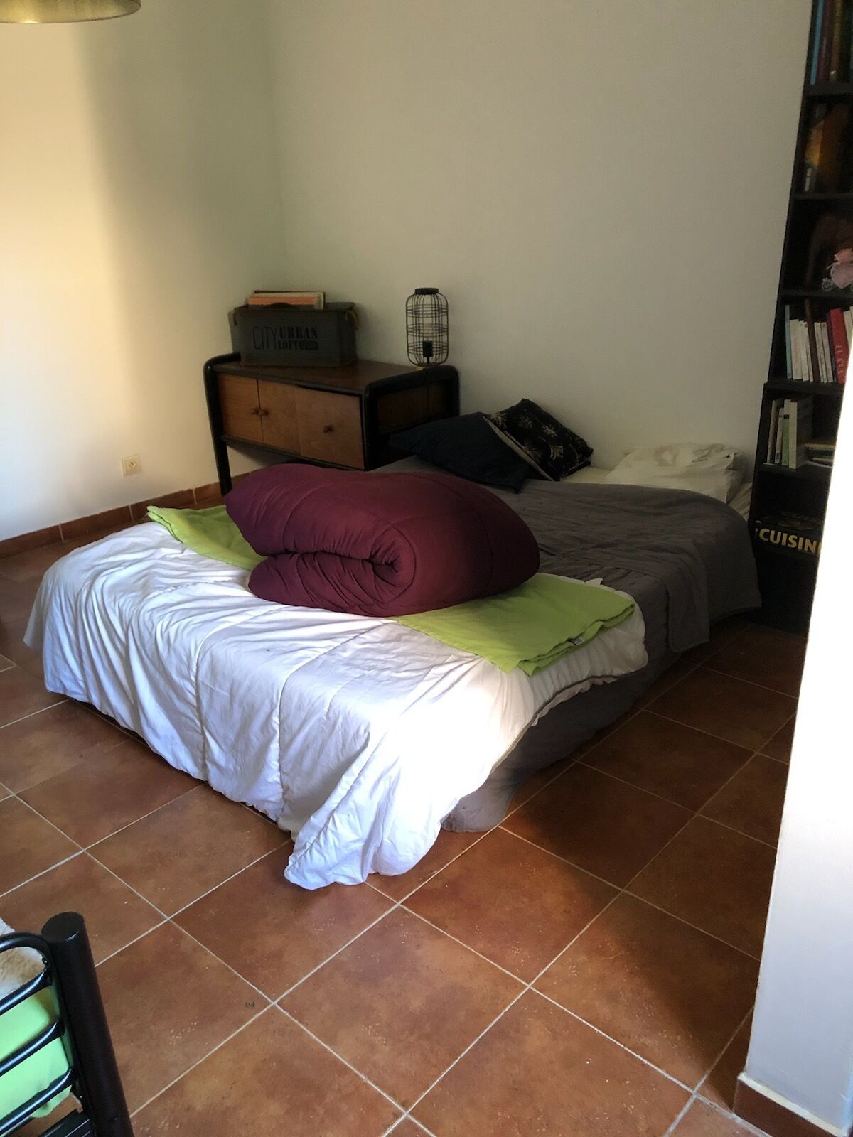 A bedroom with a bed, a nightstand, a dresser, a bookshelf, and a tiled floor.