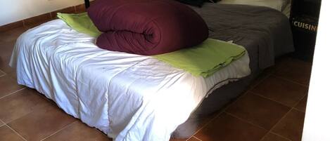 A bedroom with a bed, a nightstand, a dresser, a bookshelf, and a tiled floor.