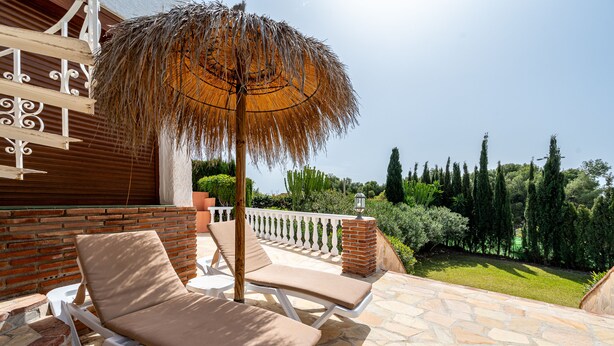 Eine Terrasse mit zwei Liegestühlen, einem Reedschirm und einer Ziegelwand.