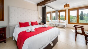 Ein geräumiges Schlafzimmer mit einem großen Bett, einer hölzernen Bank und Blick auf Grün durch große Fenster.