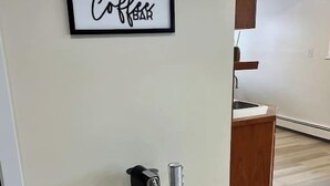 A modern kitchen with a coffee machine on a small table, a wooden cabinet, and a sign that reads "Coffee Bar".
