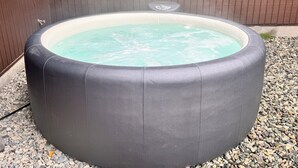 A round, black outdoor hot tub with a white interior, surrounded by pebbles and a wooden fence.