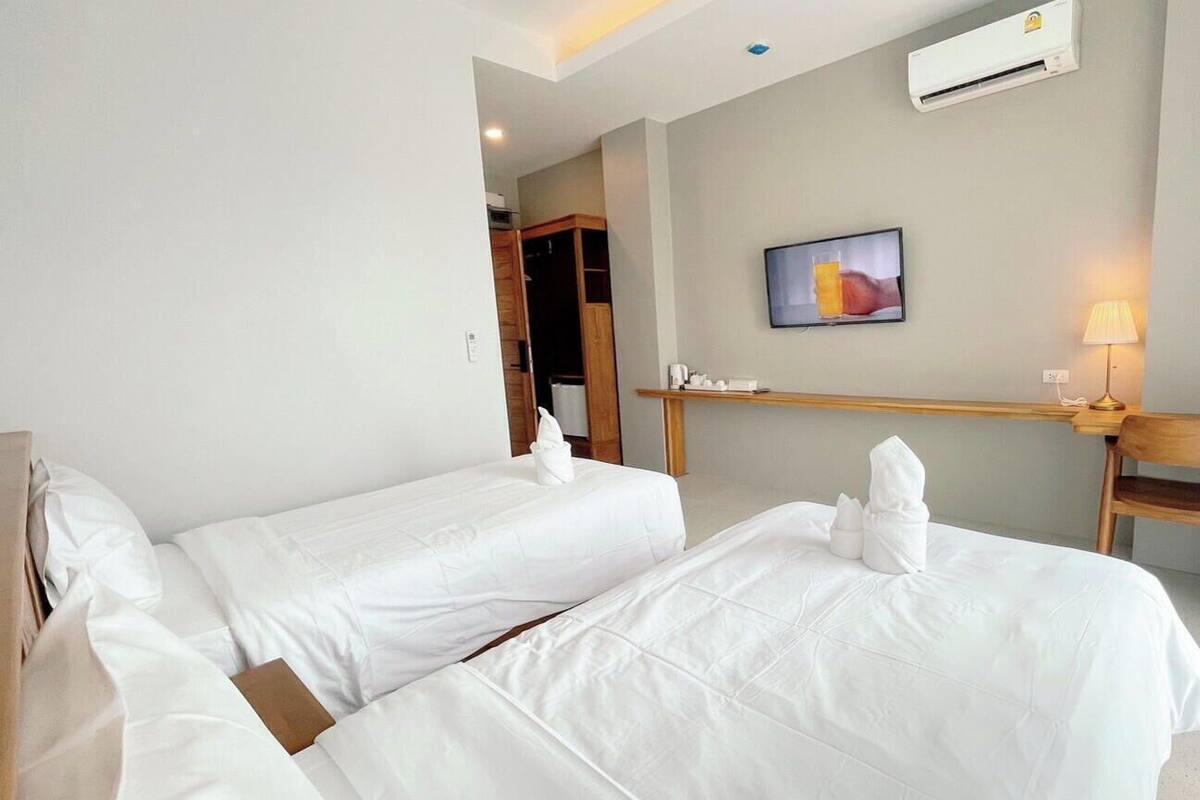 Habitación de hotel con dos camas, un escritorio, una silla, un equipo de aire acondicionado y un cuadro en la pared.