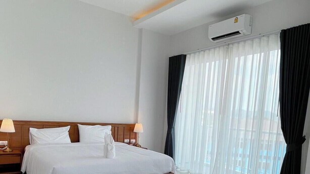 Quarto de hotel com cama, duas luminárias de cabeceira, ar condicionado e janela com cortinas.