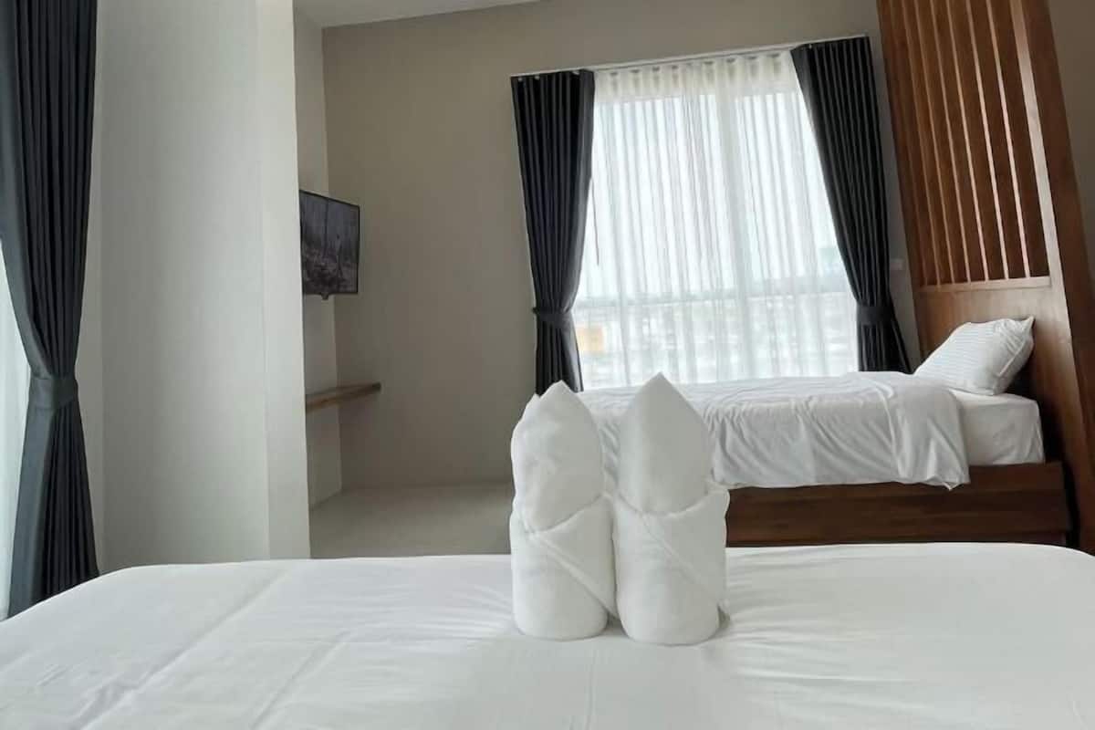 Una habitación de hotel con cama, cabecera y ventana con cortinas.