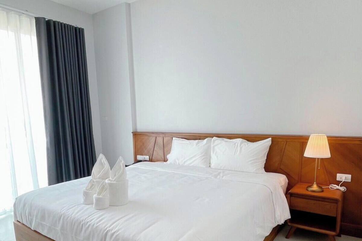 Habitación de hotel con una cama grande, una mesita de noche con lámpara y vistas al exterior.