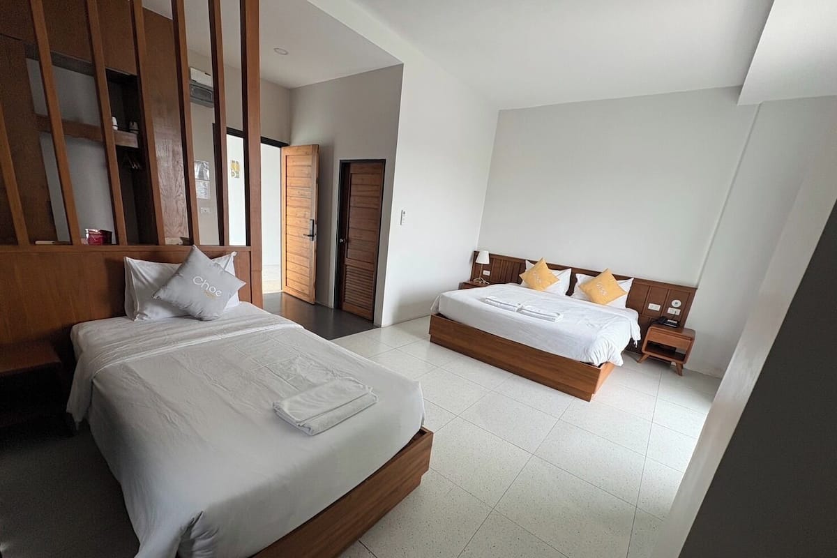 Habitación de hotel con dos camas, cabeceros de madera, ropa de cama blanca y suelo de baldosas.