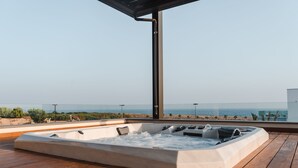 Un bain à remous sur une terrasse en bois, avec vue sur la plage et l’océan.