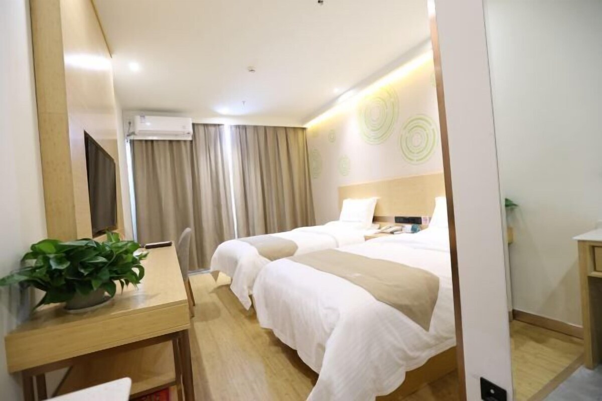 A hotel room with two beds, a desk with a plant, a TV, and a window with curtains.