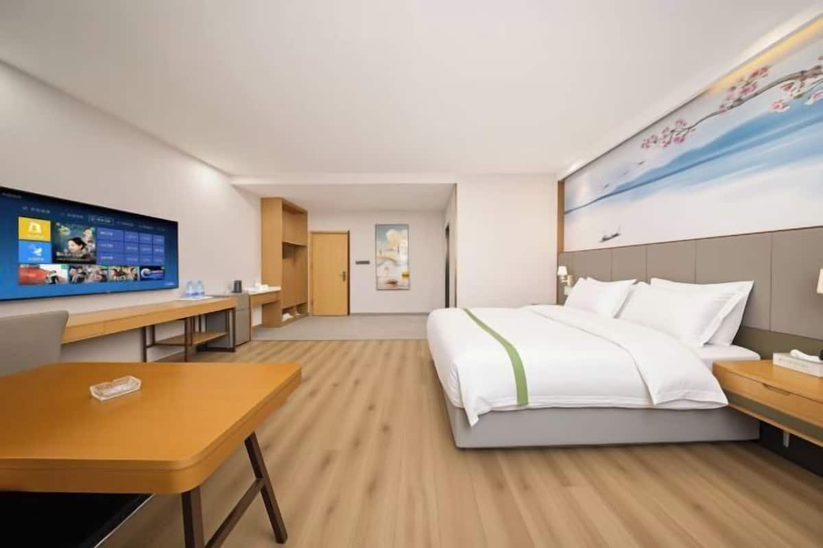 Hotellihuone, jossa on sänky, työpöytä, televisio ja taulu seinällä.