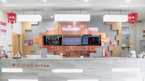 A reception desk with a digital screen, a wooden accent wall, and a tiled floor. - GreenTree Zhixuan Hotel (Dezhou Bus Train Station Black Horse Antiques Debai Plaza) (Dezhou)